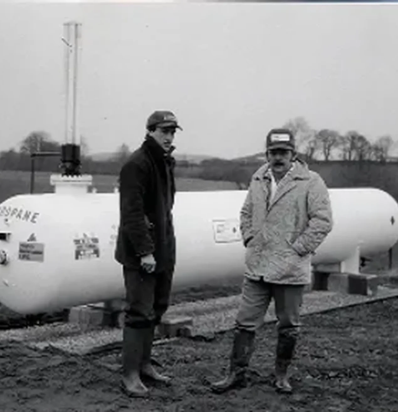 2 men standing infront of an LPG gas tank